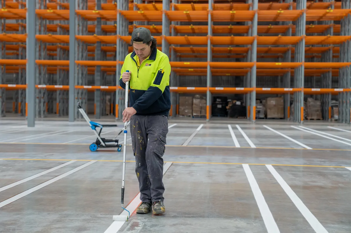 Technician applying precise white warehouse storage lines in Melbourne's west